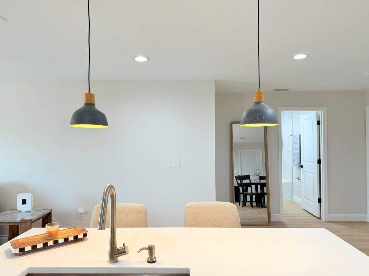 A modern kitchen with a central island, two pendant lights, and a view into a dining area.
