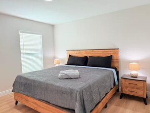 A bedroom with a wooden bed frame, grey bedding, two bedside lamps, and a wooden nightstand with drawers.