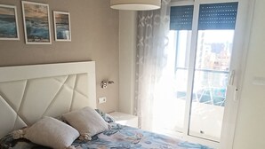 Una camera da letto con un letto, un comodino, una finestra con tende e vista sugli edifici.