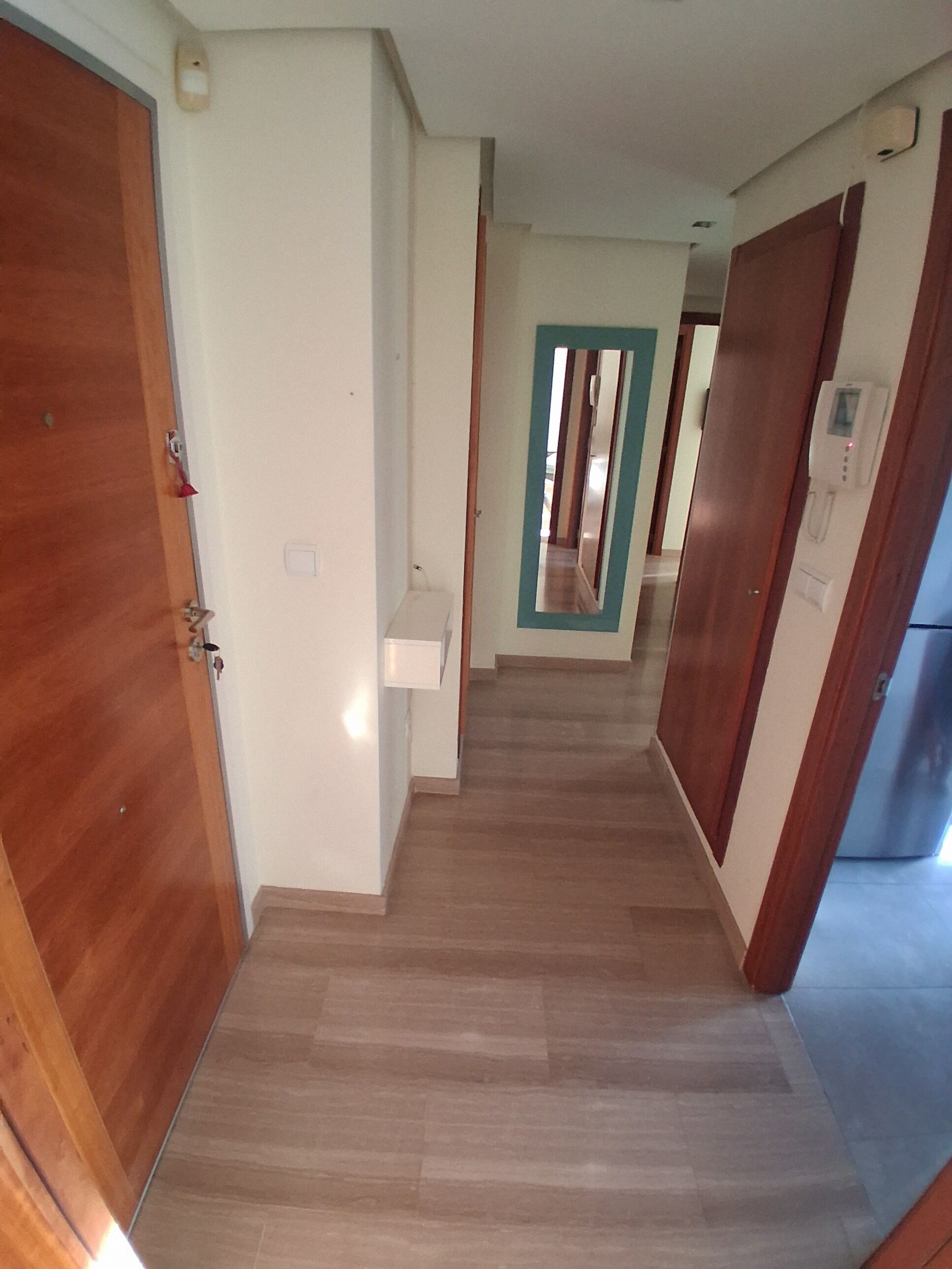 Un pasillo con puertas de madera, una pared blanca y suelo de baldosas.