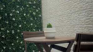 A patio area with a round table and wooden chairs, a potted plant, and a textured wall. - Cozy 1-bedroom apartment with terrace in Dakar (Dakar)