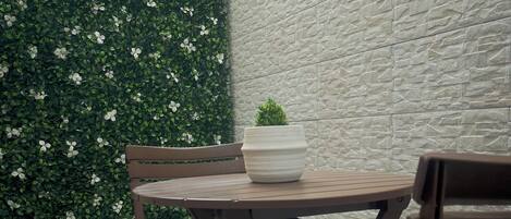 A patio area with a round table and wooden chairs, a potted plant, and a textured wall.