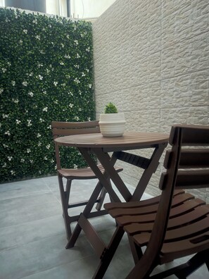A patio area with a round table and wooden chairs, a potted plant, and a textured wall. - Cozy 1-bedroom apartment with terrace in Dakar (Dakar)