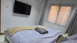 A bedroom with two beds, a television mounted on the wall, and a window with curtains. - Cozy 1-bedroom apartment with terrace in Dakar (Dakar)