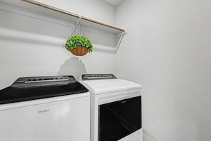 Una sala de bugaderia amb dues rentadores Whirlpool i una planta penjant.