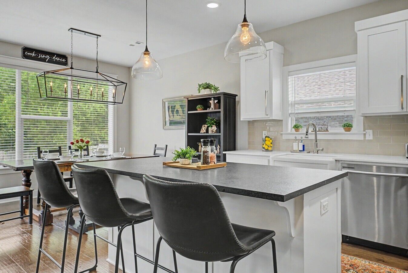 A modern kitchen with a central island, bar stools, pendant lighting, and a view of the outdoors.