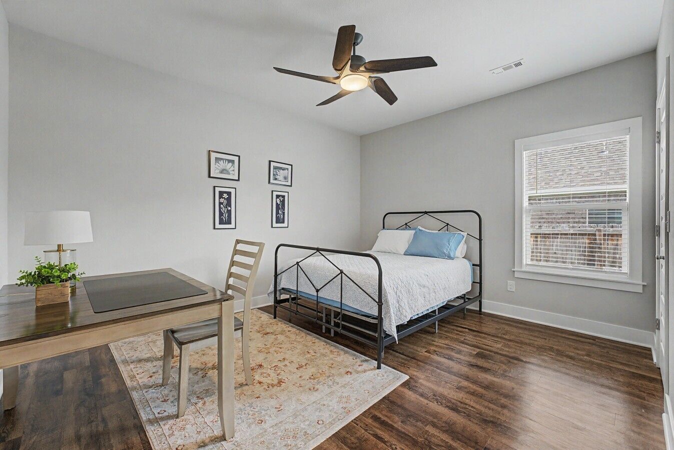 Quarto com cama, escrivaninha, cadeira, ventilador de teto e janela com persianas.