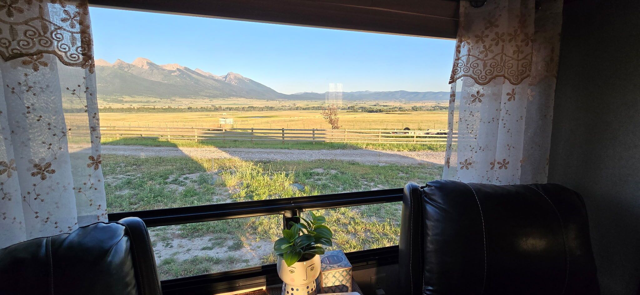 Ein Zimmer mit Blick auf eine gebirgige Landschaft durch ein Fenster, eine Pflanze auf einem Tisch und zwei Ledersessel.