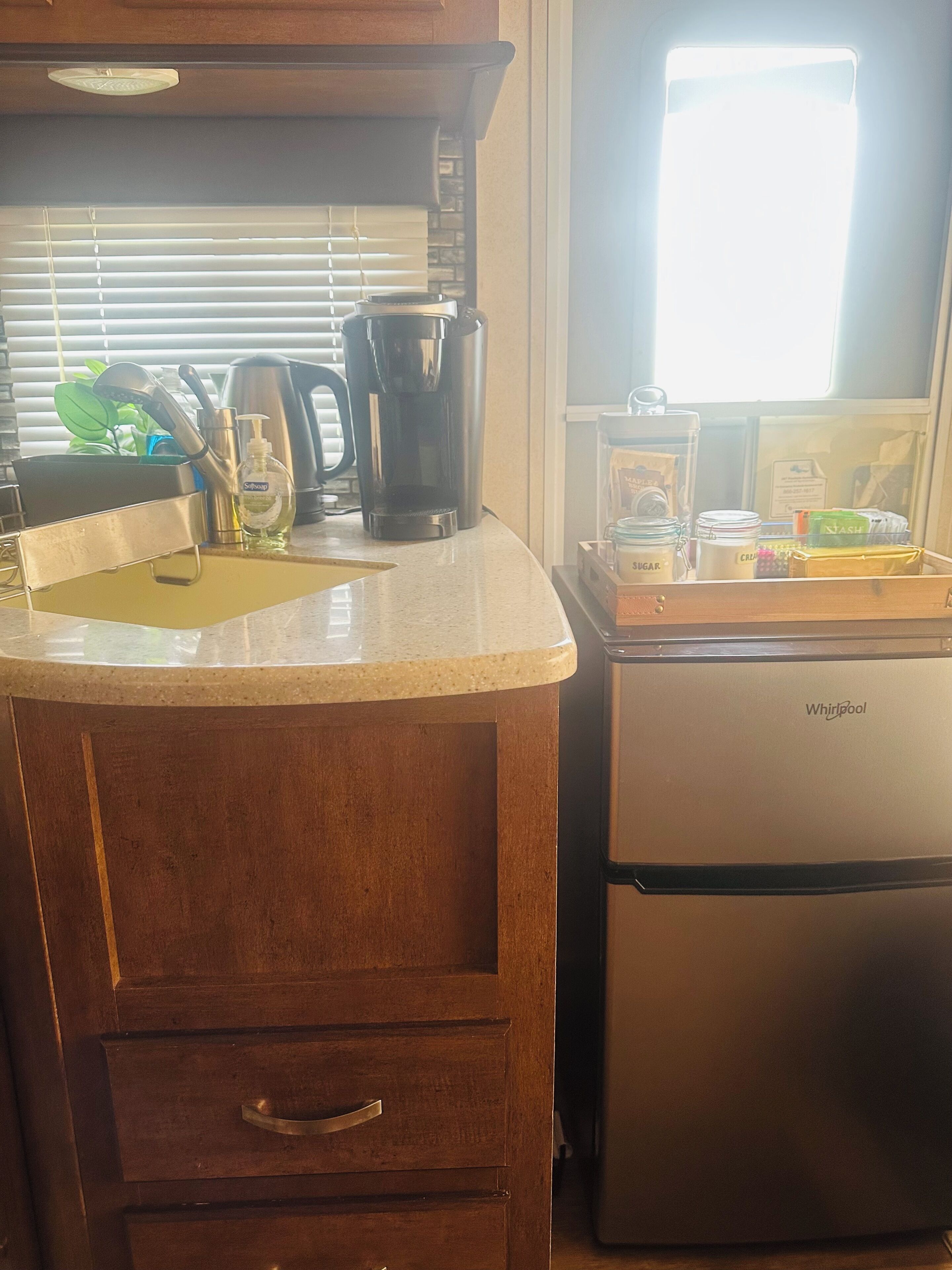 A kitchen with a countertop, a coffee maker, a kettle, and a refrigerator.