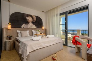 Ein Hotelzimmer mit Bett, einem Bild an der Wand, einem Balkon mit Aussicht und einem Sessel.