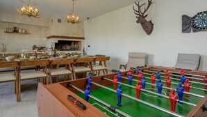 Ein Essbereich mit Holztisch und Stühlen, einem Kicker, einem Kamin und einem aufgehängten Hirschkopf.
