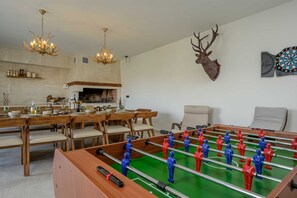 Ein Essbereich mit Holztisch und Stühlen, einem Kicker, einem Kamin und einem aufgehängten Hirschkopf.