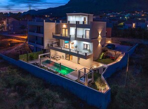 Ein modernes mehrstöckiges Haus mit Swimmingpool, Sitzgelegenheiten im Freien und einer Treppe, die zu einem Balkon führt.