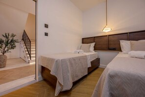 Quarto de hotel com duas camas, cabeceira de madeira, planta em vaso e uma escada.