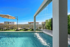Ein Schwimmbecken mit Wasserspiel, Liegestühlen und Blick auf Gebäude im Hintergrund.