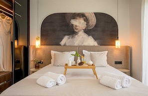 Habitación de hotel con una cama grande, dos mesitas de noche, una bandeja con alimentos para el desayuno y un cuadro sobre la cama.