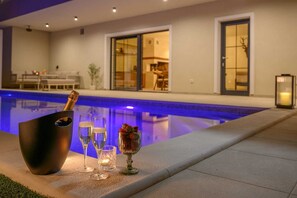 Cenário junto à piscina com uma garrafa de champanhe, copos e um vaso decorativo.