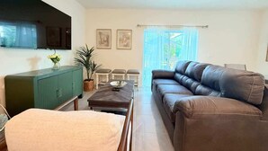 Una sala de estar con un sofá de cuero marrón, un mueble verde, una mesa de comedor con sillas y un televisor en la pared.