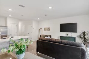 A modern living room with a sofa, a flat-screen TV, a dining area, and a kitchen. - Tamarack Magic 3/2 Luxury & Magic Near Disney (Davenport)