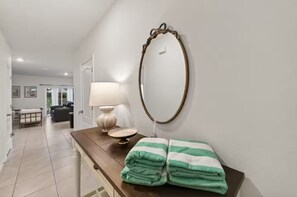A hallway with a wooden bench, a lamp, a mirror, and a door leading to a living area. - Tamarack Magic 3/2 Luxury & Magic Near Disney (Davenport)