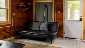 Une pièce avec un canapé en cuir noir, un mur en bois, une porte et une fenêtre.