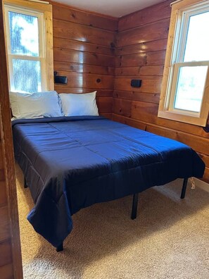 Ein Schlafzimmer mit einem Bett, zwei Kissen, Holzwänden und einem Fenster.