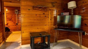 L’intérieur d’un chalet en bois, avec un téléviseur posé sur un meuble, une petite table et une lampe.