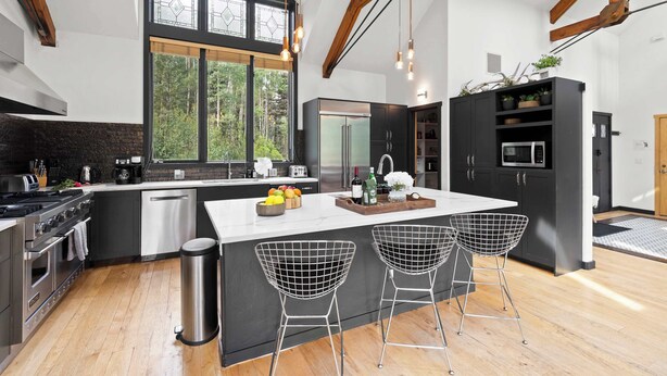 Cocina moderna con una isla grande, electrodomésticos de acero inoxidable y vistas al bosque.
