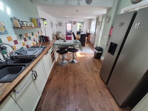 A kitchen with a central island, bar stools, and a refrigerator. - 19 Newtown Sidmouth is a Cosy Cottage and Family Home 600m to Beach (Sidmouth)