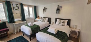 A hotel room with two beds, a vanity with a mirror, a window with curtains, and wall-mounted decor. - 19 Newtown Sidmouth is a Cosy Cottage and Family Home 600m to Beach (Sidmouth)