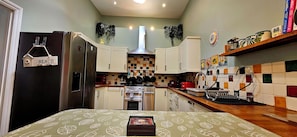 A compact kitchen with a refrigerator, stove, and microwave. There are cabinets, a sink, and a countertop with various items. - 19 Newtown Sidmouth is a Cosy Cottage and Family Home 600m to Beach (Sidmouth)