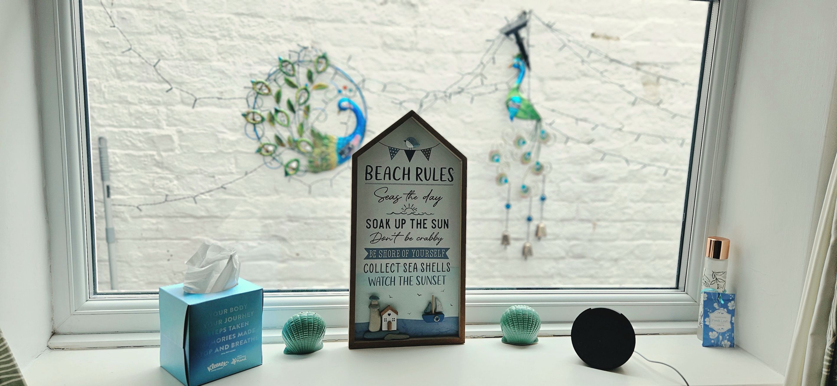 A framed inspirational quote on a window ledge with a tissue box and decorative items beside it.