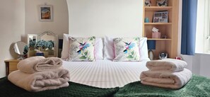 A neatly made bed with two pillows, a bedside table with a mirror, and a shelf with personal items. - 19 Newtown Sidmouth is a Cosy Cottage and Family Home 600m to Beach (Sidmouth)