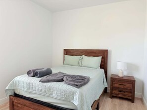 Uma cama bem arrumada com cabeceira, uma mesa de cabeceira com abajur e um criado-mudo de madeira.