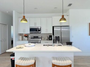 A modern kitchen with white cabinetry, stainless steel appliances, and pendant lighting.