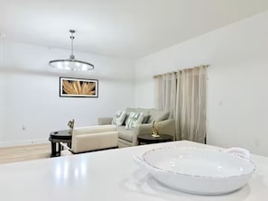 Una sala de estar moderna con un sofá blanco, una mesa redonda de centro, una lámpara colgante y un cuadro enmarcado en la pared.