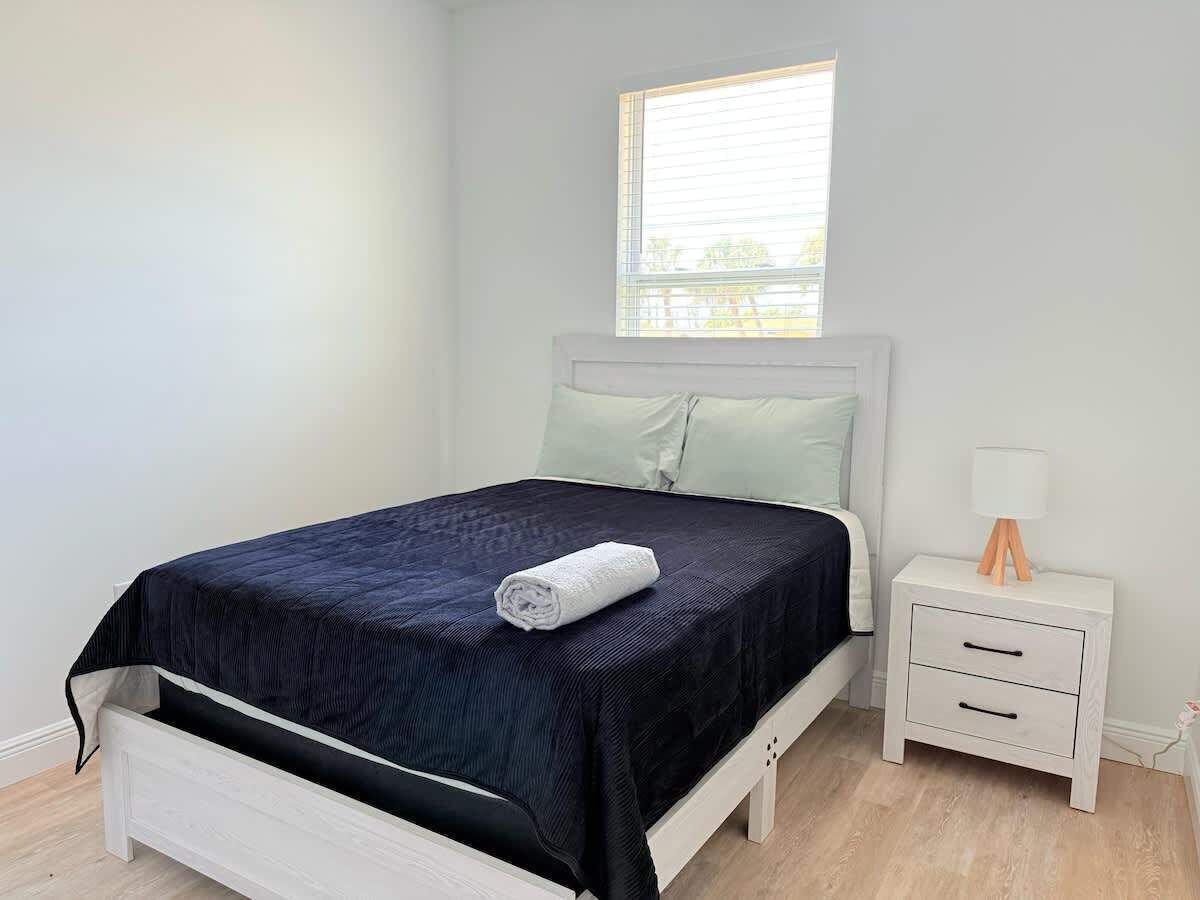 A bed with a dark blue bedspread, a white headboard, and a window above it.