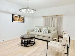 A living room with a sofa, a round table, a chair, and a pendant light.
