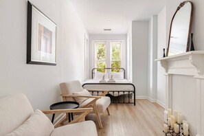 A modern bedroom with a bed, two chairs, a small table, a fireplace, and a large mirror. - Modern &Historic Northwest Charm (Washington)
