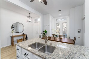 A modern kitchen with granite countertops, a double sink, and a dining area with a table and chairs. - Modern &Historic Northwest Charm (Washington)