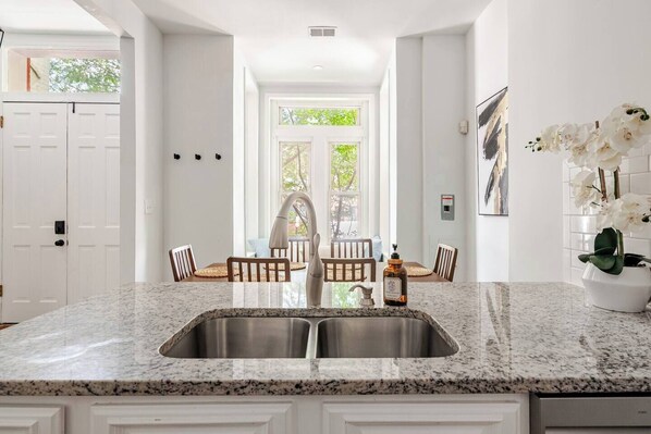 A kitchen with a granite countertop, stainless steel sink, and wooden chairs. - Modern &Historic Northwest Charm (Washington)