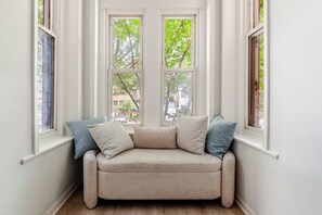 A corner room with a beige sofa, two windows, and a view of trees. - Modern &Historic Northwest Charm (Washington)