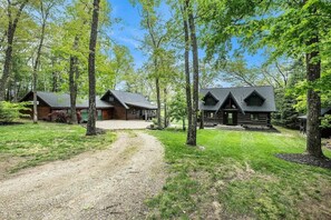 A rustic cabin-style lodging with a gravel driveway, surrounded by tall trees and a clear sky.