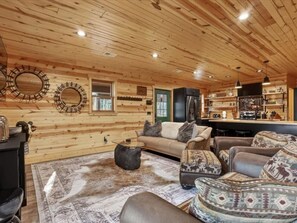 A log cabin interior with a sofa, coffee table, and patterned ottoman.