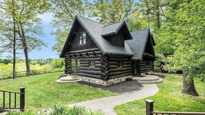 Een vakantiehuisje van hout met een steil dak, omringd door een verzorgd gazon en bomen.