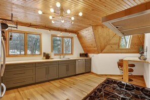 A kitchen with wooden floors, a stove, and a window overlooking a snowy landscape.