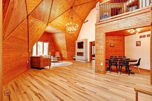 A spacious loft with wooden floors, a dining area, a fireplace, and a balcony.