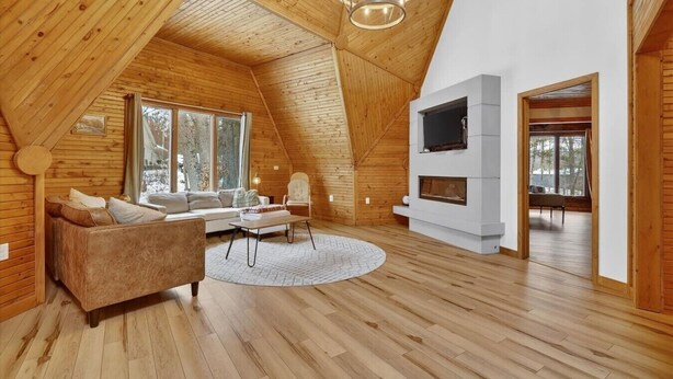Un loft espacioso con techo alto, paredes de madera, un ventanal grande, un sofá, una silla, una chimenea y un televisor.