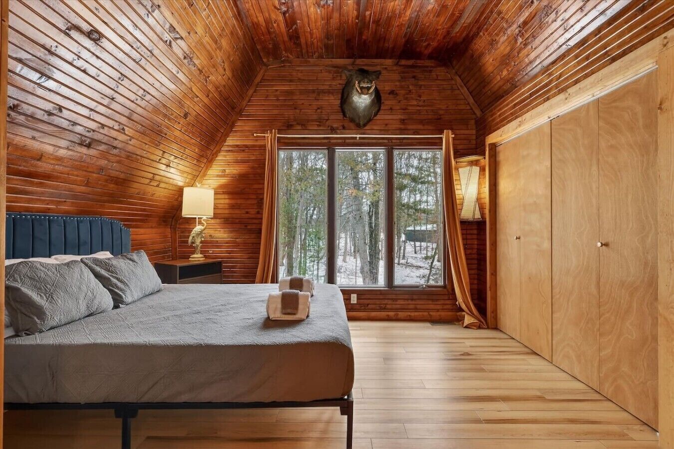 A log cabin bedroom with a bed, bedside lamp, and a window with curtains.