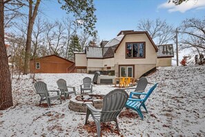 A house with a fire pit and outdoor seating, surrounded by snow.